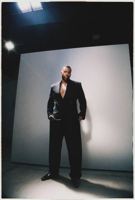 Portrait of an African American man in a suit posing in a photo studio with a white backdrop, showcasing fashion and style.