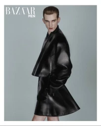 Model Eugen Ivanov posing in a structured black leather coat against a soft pale blue-grey seamless studio backdrop.
