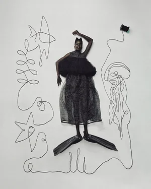 A Black female model in a sheer black dress and diving fins lies surrounded by line art made from black yarn on a light background.