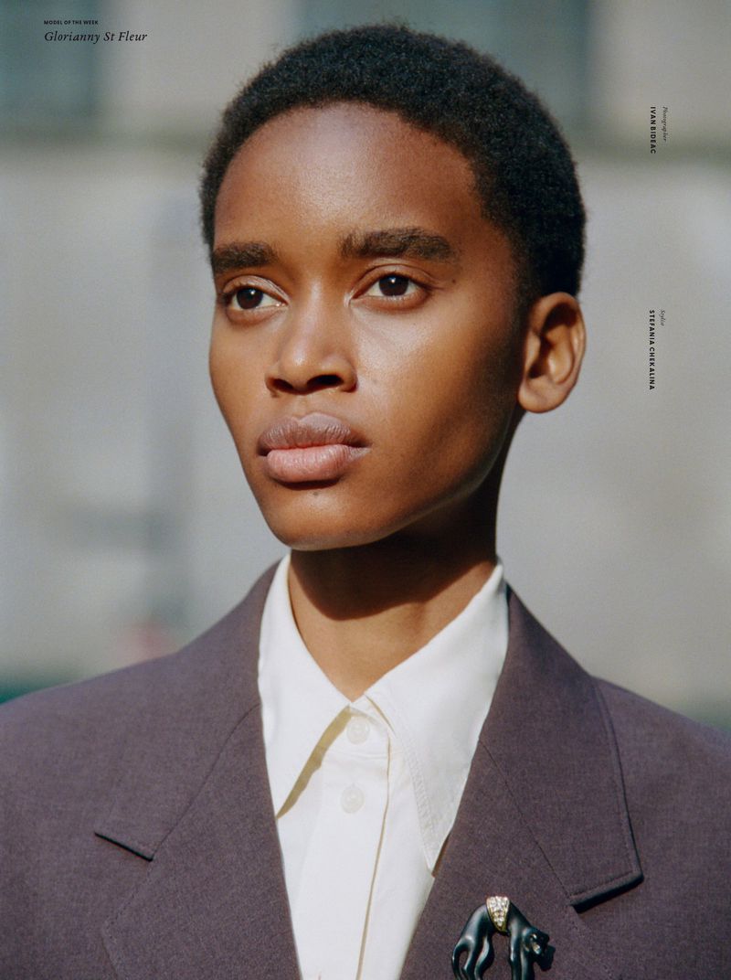 Close-up portrait of a Black woman with short hair wearing a brown blazer, collared shirt, and an animal brooch. Natural lighting.