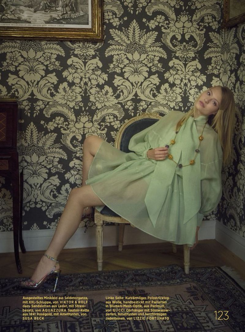 Woman in green dress and heels poses against floral wallpaper and antique furniture in an indoor fashion shot for editorial.