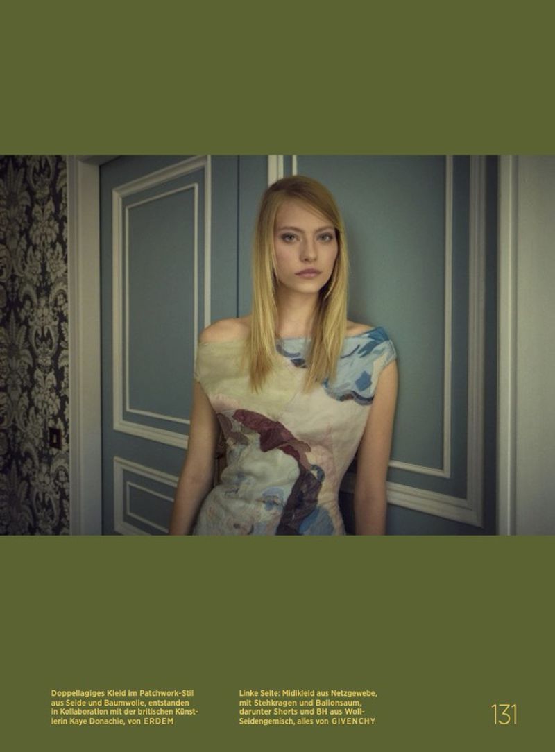 Fashion editorial shot of a blonde model in a printed dress against a blue door and patterned wall, studio lighting, medium shot.