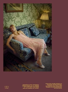 Model wearing a pink fringed dress lounging on a blue patterned sofa in a vintage-style room