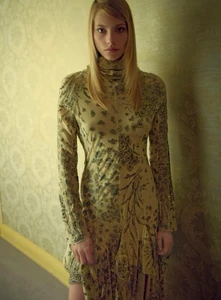 Annie Arnander wearing a long-sleeved floral turtleneck dress standing against a patterned wallpaper wall.