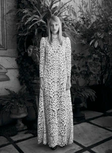 Model Annie Arnander wearing an intricate high-neck white lace maxi dress in an outdoor garden courtyard.