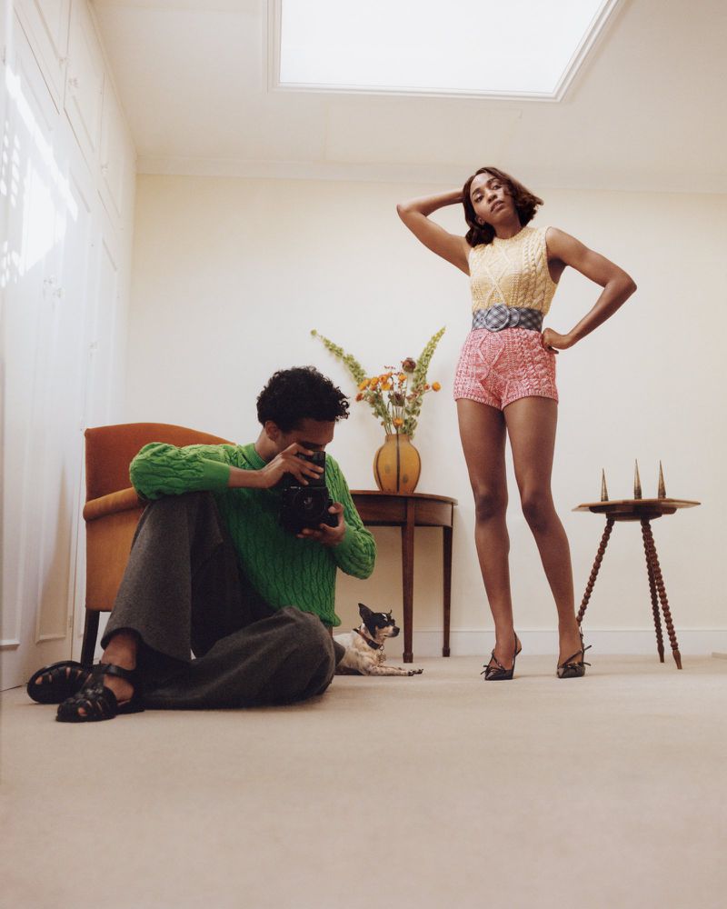 A fashion editorial image features an adult male taking a photo with a vintage camera and an adult female posing indoors with props.