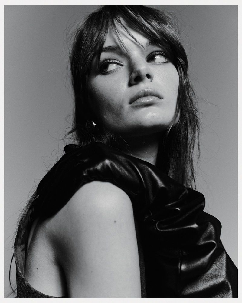 Monochrome portrait of a young adult woman with dark hair looking away, posing in a studio with a black top, showcasing beauty and style.