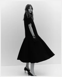 Monochrome fashion portrait of a model wearing a black dress and heels against a plain white background for H&M TAILORING HOLIDAY.