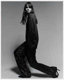 Model in dark satin shirt and sequined trousers posing against a grey studio backdrop for H&M TAILORING HOLIDAY.