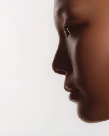 Extreme close-up profile portrait of a woman's face in soft shadow against a bright white studio backdrop.