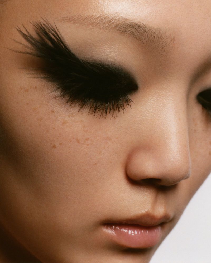 Close-up portrait of a woman with dramatic black feathered eyelashes and neutral-toned skin, emphasizing beauty and fashion.