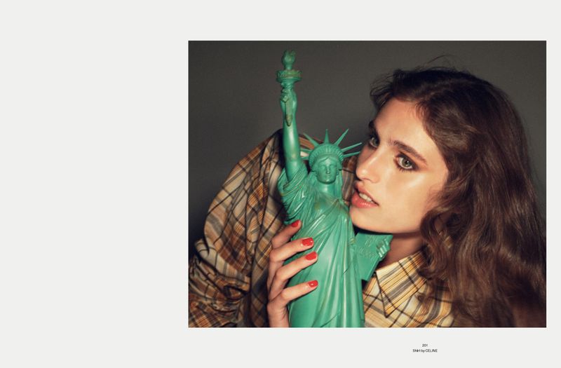 Adult female embraces Statue of Liberty figurine in a close-up studio shot with a blurred, warm-toned plaid shirt in the backdrop.