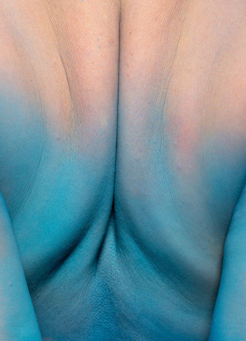 Close-up of a woman's back featuring skin that transitions from fair to a vibrant turquoise through body paint, creating an abstract visual.