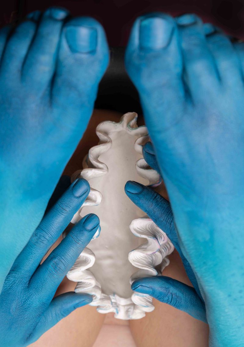 Close-up of a fair-skinned person with blue painted hands and feet holding a decorative plaster object with ruffled edges.