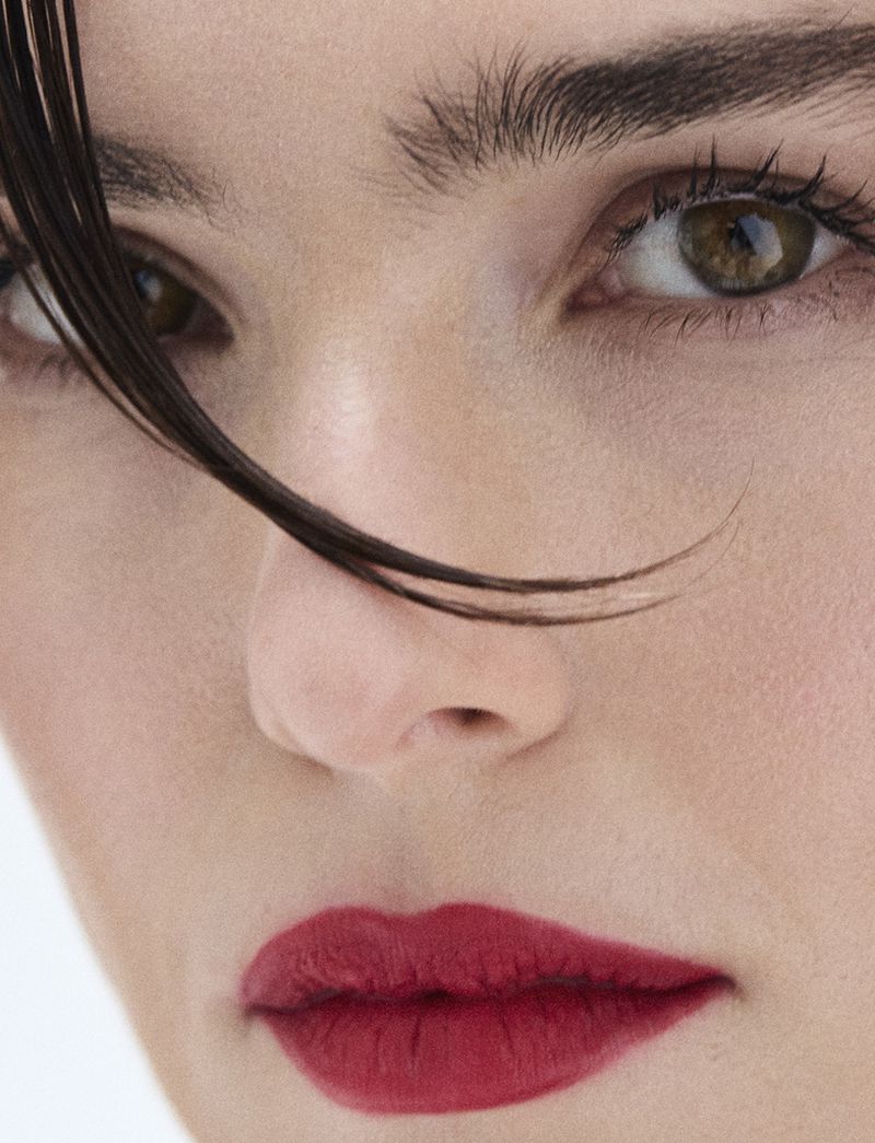 Close-up of a woman's face showcasing red lipstick, light skin, and brown eyes, with dark hair framing her face. Beauty shot. 