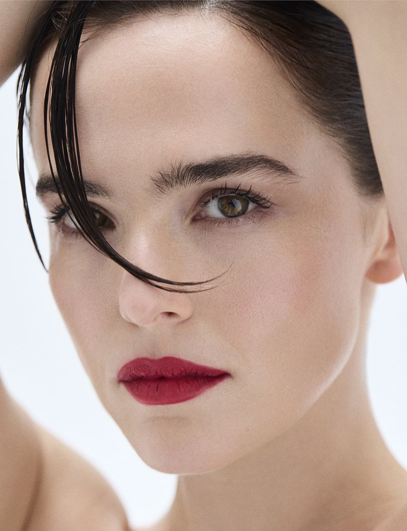 Close-up portrait of a woman with red lipstick and dark hair, posing in a brightly lit indoor setting, showcasing her beauty.