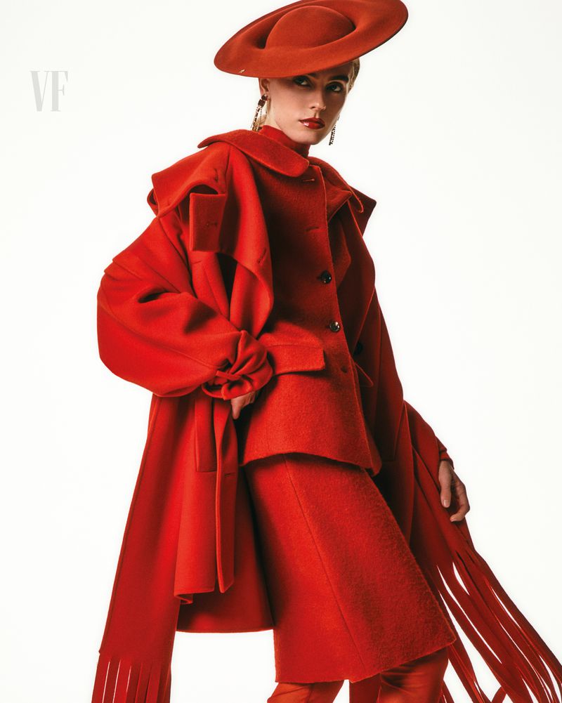 Fashion editorial shot of a model in a vibrant red coat, hat, and pants against a bright white backdrop, high-fashion statement.