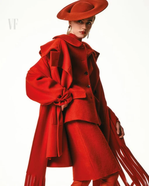 Fashion editorial shot of a model in a vibrant red coat, hat, and pants against a bright white backdrop, high-fashion statement.