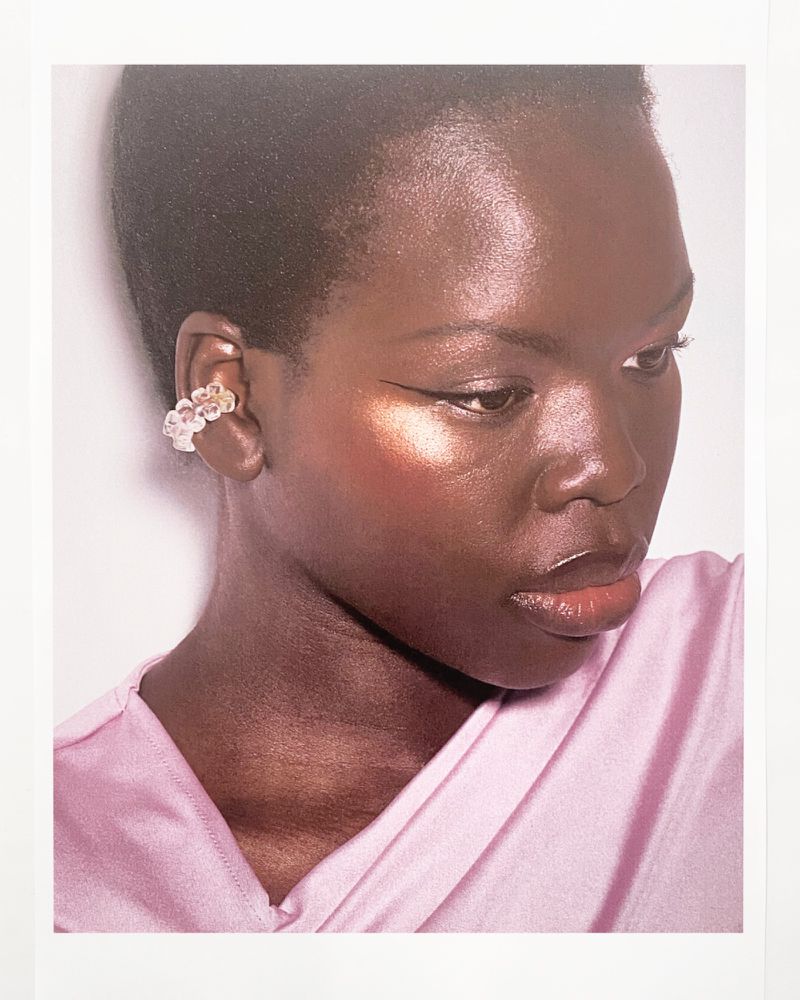Close-up portrait of a Black woman with short dark hair wearing a pink top and a unique floral ear cuff, gazing downwards.