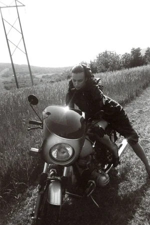 Model Irina Shayk leaning over a motorcycle on a grassy roadside hill for Self Service magazine.