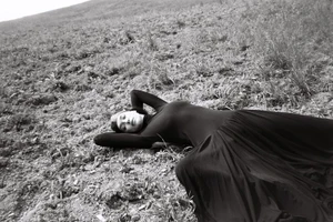 Model Irina Shayk reclining on a grassy earth hillside wearing a long black gown in a black and white fashion editorial.