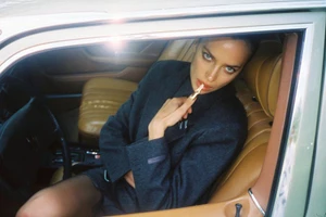 Irina Shayk wearing a dark grey oversized blazer inside a vintage car with tan leather seats.