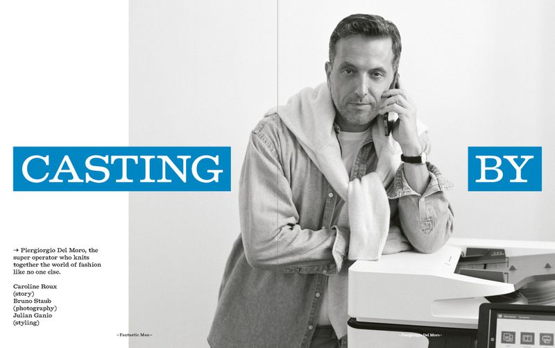 Portrait of an adult male talking on a cellphone, wearing a denim shirt and sweater, leaning on an office machine, indoors.