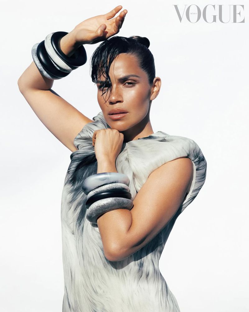 Fashion portrait of a woman in an abstract dress and chunky black and silver bracelets against a bright white background, with Vogue logo.