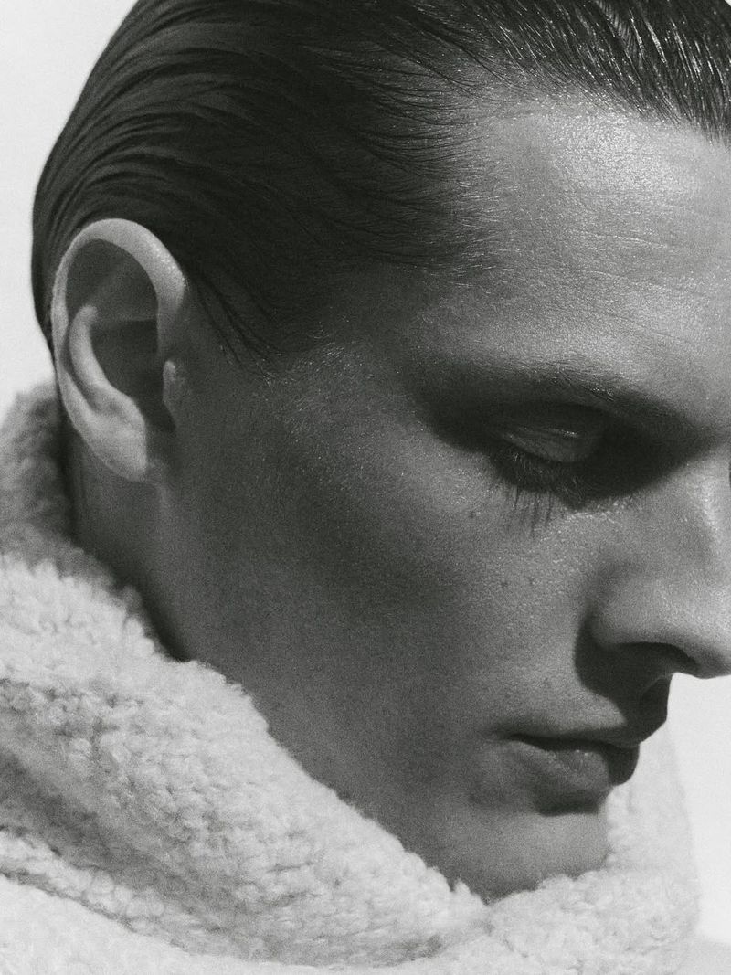 Black and white portrait of an adult male with slicked-back hair and a fluffy white collar, captured in a close-up shot with even lighting.