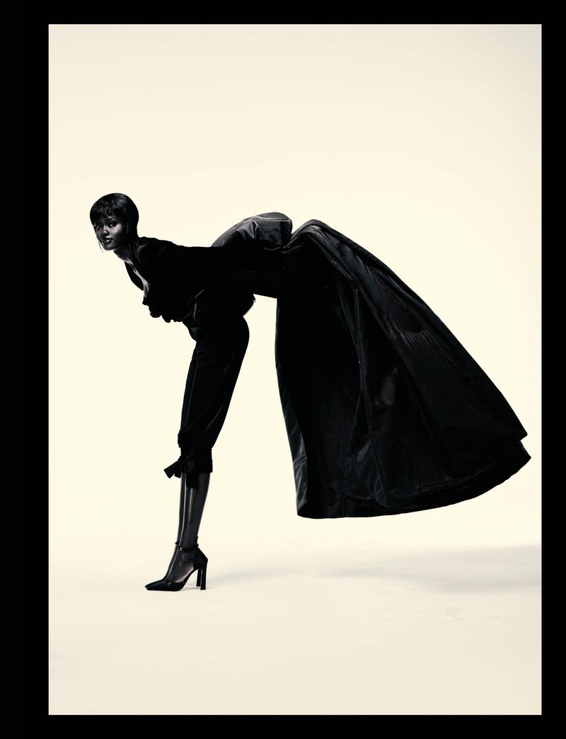 Fashion shoot featuring a Black female model in a sculptural black outfit, posed against a neutral backdrop in a studio setting.