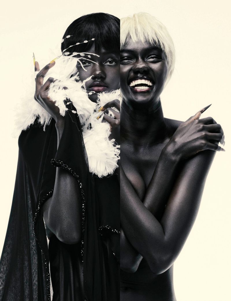 Striking fashion portrait featuring two women with dramatic makeup, wigs, and costumes against a cream background in a studio setting.