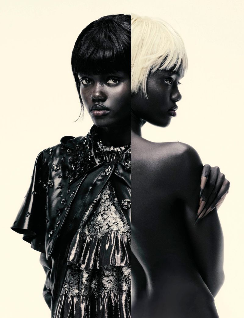 Striking studio portrait features two dark-skinned women. One wears a layered, ruffled dress with lace, while the other is nude, revealing her back.