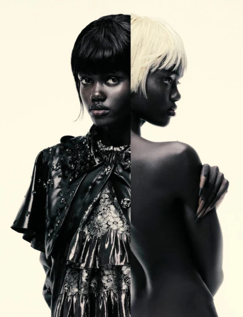 Striking studio portrait features two dark-skinned women. One wears a layered, ruffled dress with lace, while the other is nude, revealing her back.
