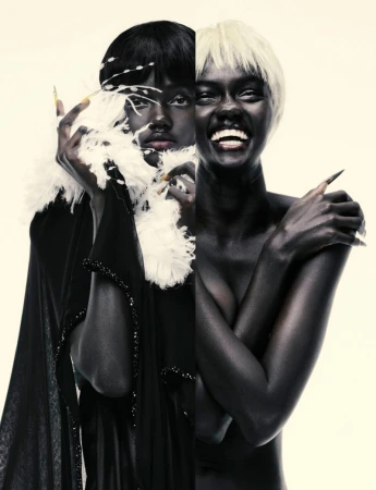 Split studio portrait of model Achol Kuir juxtaposing dark hair with a white feather boa and blonde hair with bare shoulders.