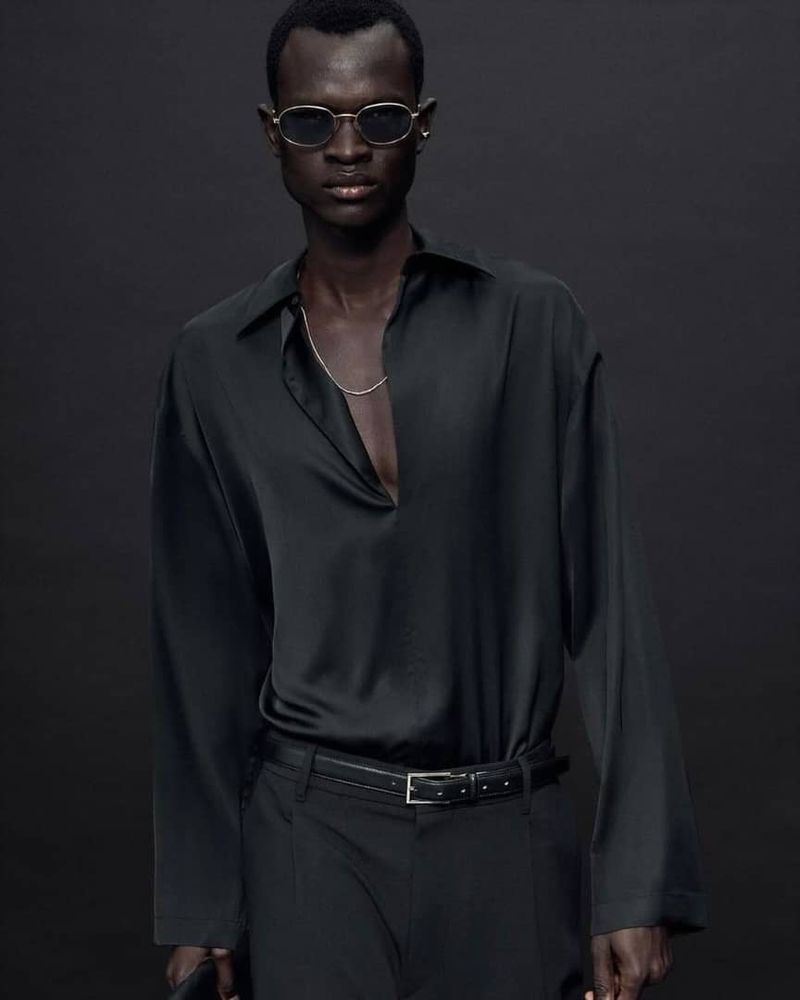 Man wearing black silk shirt and sunglasses in studio setting. Fashion shot with dark background. Elegant modern style.