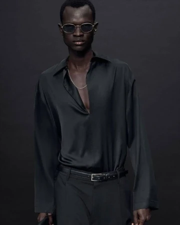Man wearing black silk shirt and sunglasses in studio setting. Fashion shot with dark background. Elegant modern style.