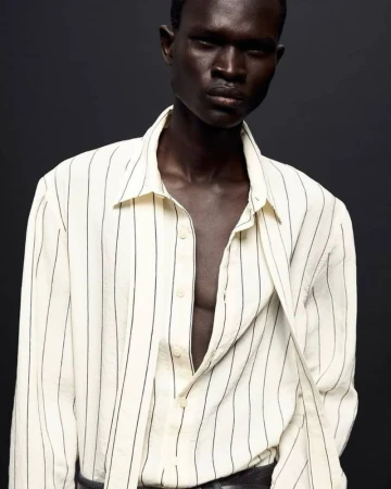 Model wearing a white and black striped long-sleeve shirt against a dark grey background for Zara Man Oct 2024 Lookbook