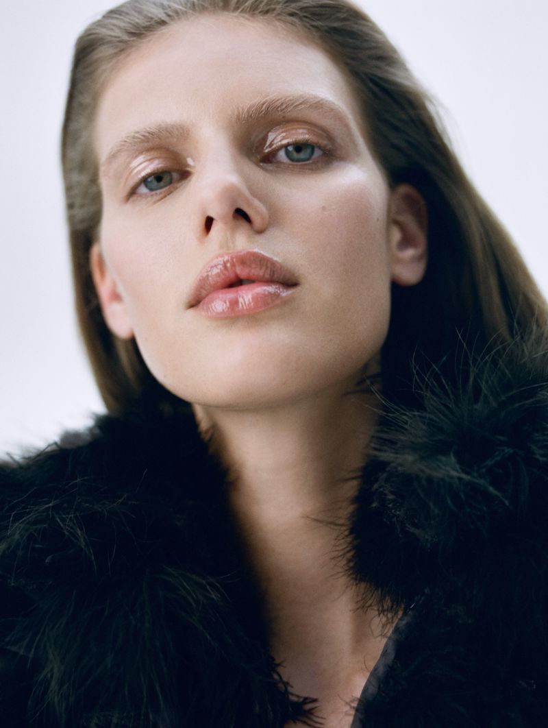 Headshot of a fair-skinned woman with blue eyes wearing a black feathered garment against a clean, bright background, showcasing beauty and style.