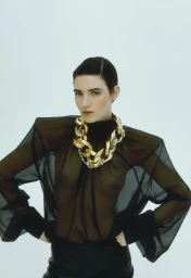 Eloise Logan in a sheer black high-neck top with structured shoulders and a chunky gold chain necklace against a white backdrop.