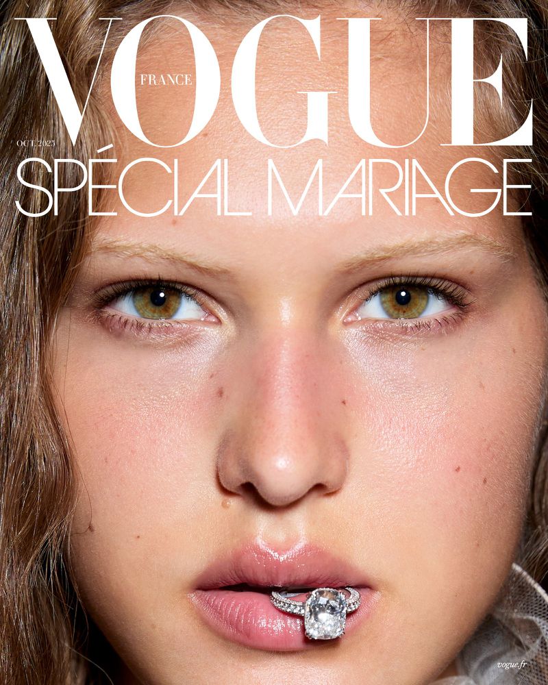 Close-up of a light-skinned adult female with light brown hair, green eyes, holding a large diamond ring in her mouth. Vogue cover.