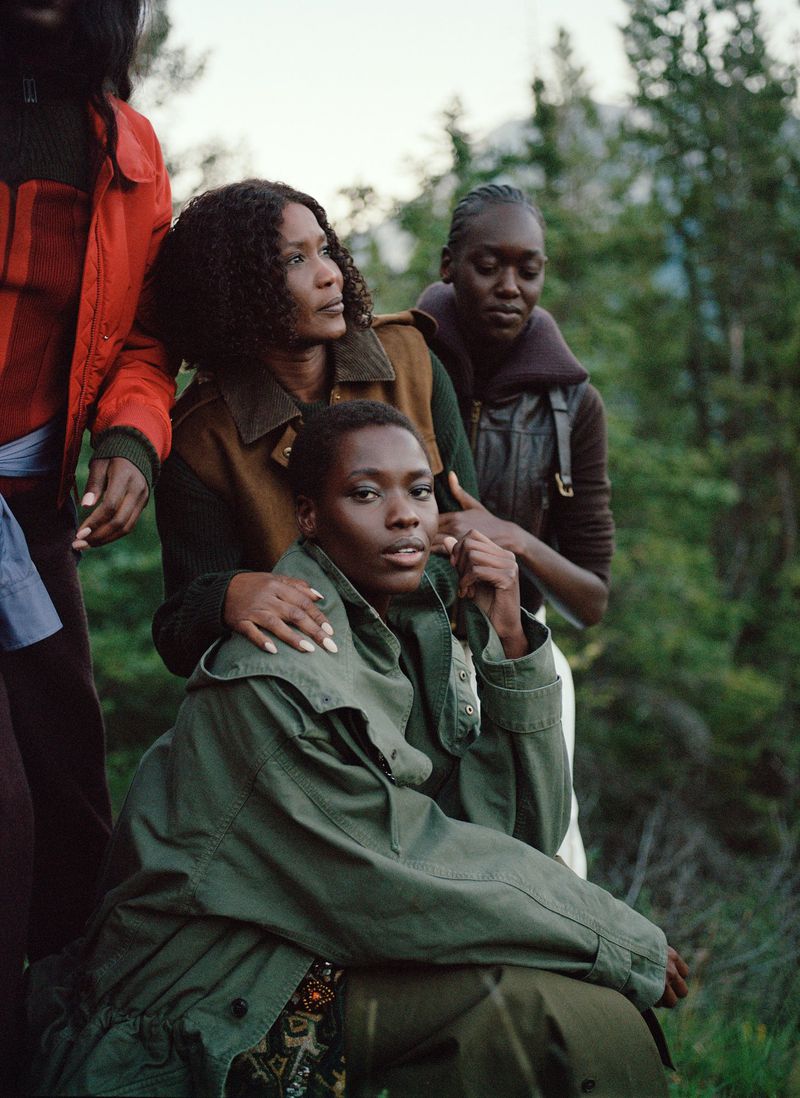 Group of four women posing together in an outdoor setting with trees and a mountain range in the background, wearing fall clothing.