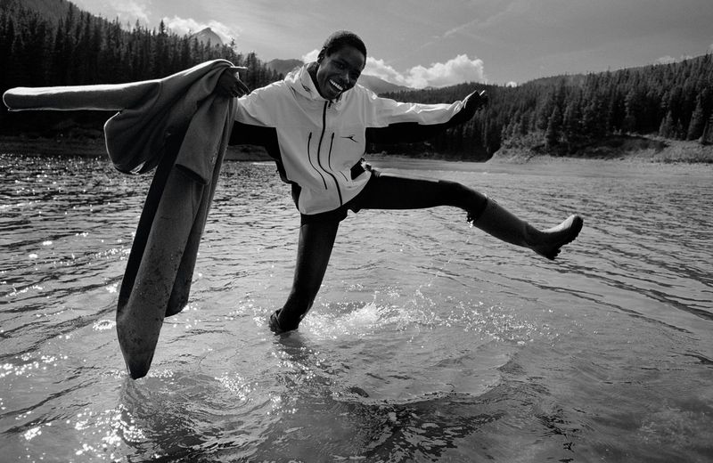 Model Awar Odhiang splashing water in a lake wearing a sports jacket holding a coat in American Vogue Outer Wilds editorial