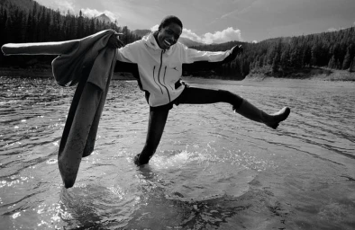 Model Awar Odhiang splashing water in a lake wearing a sports jacket holding a coat in American Vogue Outer Wilds editorial