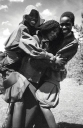 Three Black women embrace and smile together outdoors wearing outerwear jackets for American Vogue's Outer Wilds editorial.