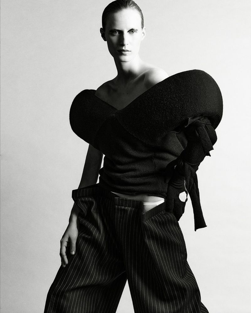 A person in a dark top and striped pants stands in a light grey studio setting, creating a high-fashion editorial image with focus on textiles.