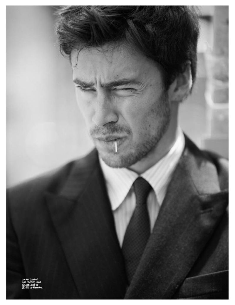 Black and white portrait of a man in a suit with a toothpick in his mouth, looking slightly off-camera with a pensive expression.