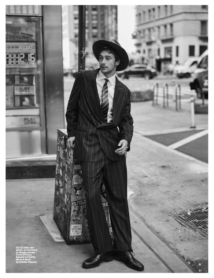 Man wearing a pinstripe suit and fedora hat posing on a city street for an Esquire US fashion editorial.