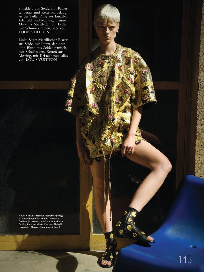 Fashion shot featuring a female model with short blonde hair wearing a gold embellished mini dress and black sandals in a studio setting.