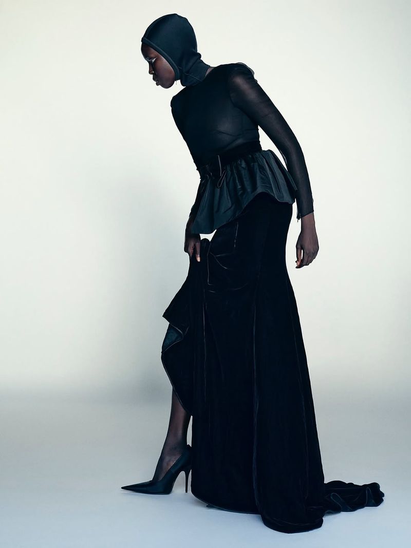 Elegant fashion shot: An adult female model in a black couture dress with sculptural details poses in a studio setting with soft lighting.