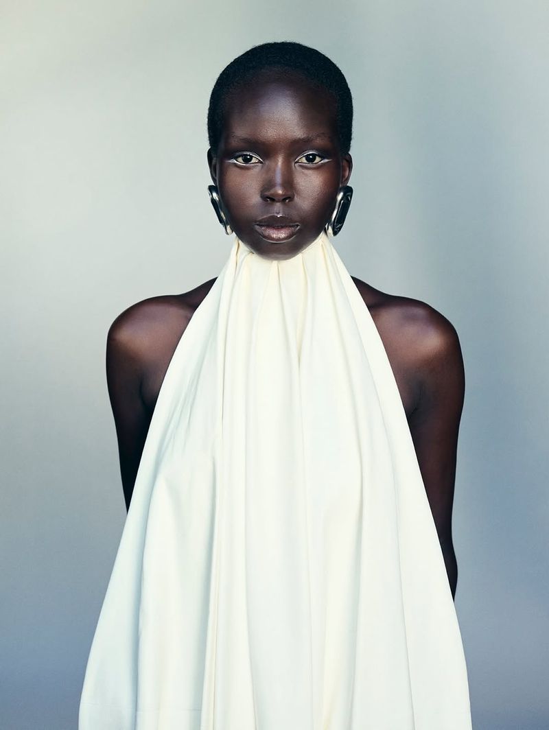 Close-up of African woman wearing a white draped halter top and oversized black earrings, against a neutral grey background in studio lighting.